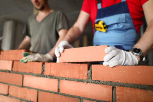 Zwei Maurer mauern eine Wand aus roten Ziegelsteinen